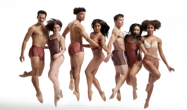 Parsons Dance Company jumps in unison, all wearing shades of brown and beige leotards and shorts